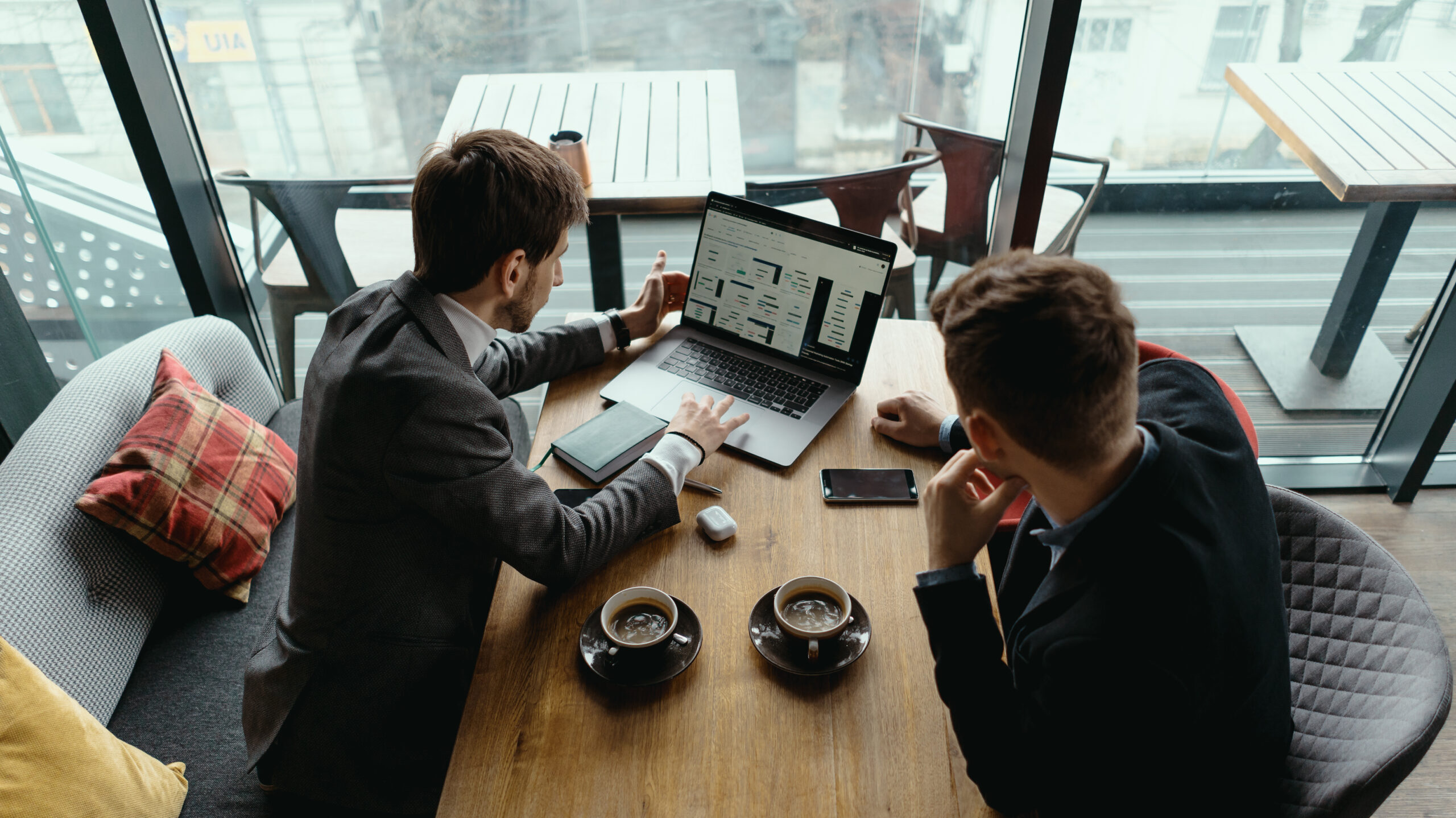 Two businessmen talking about new opportunities sitting with laptop at desk, planning project, considering business offer, sharing ideas while drinking coffee together
